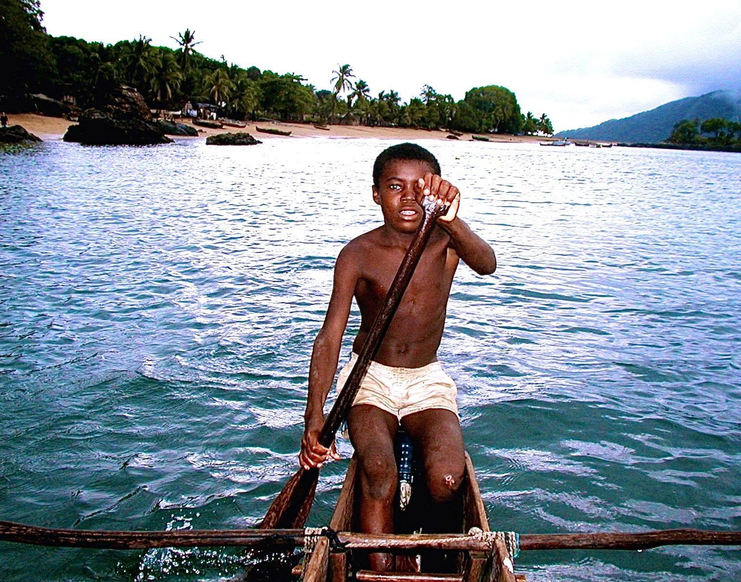 A young person paddling a wooden canoe in coastal water