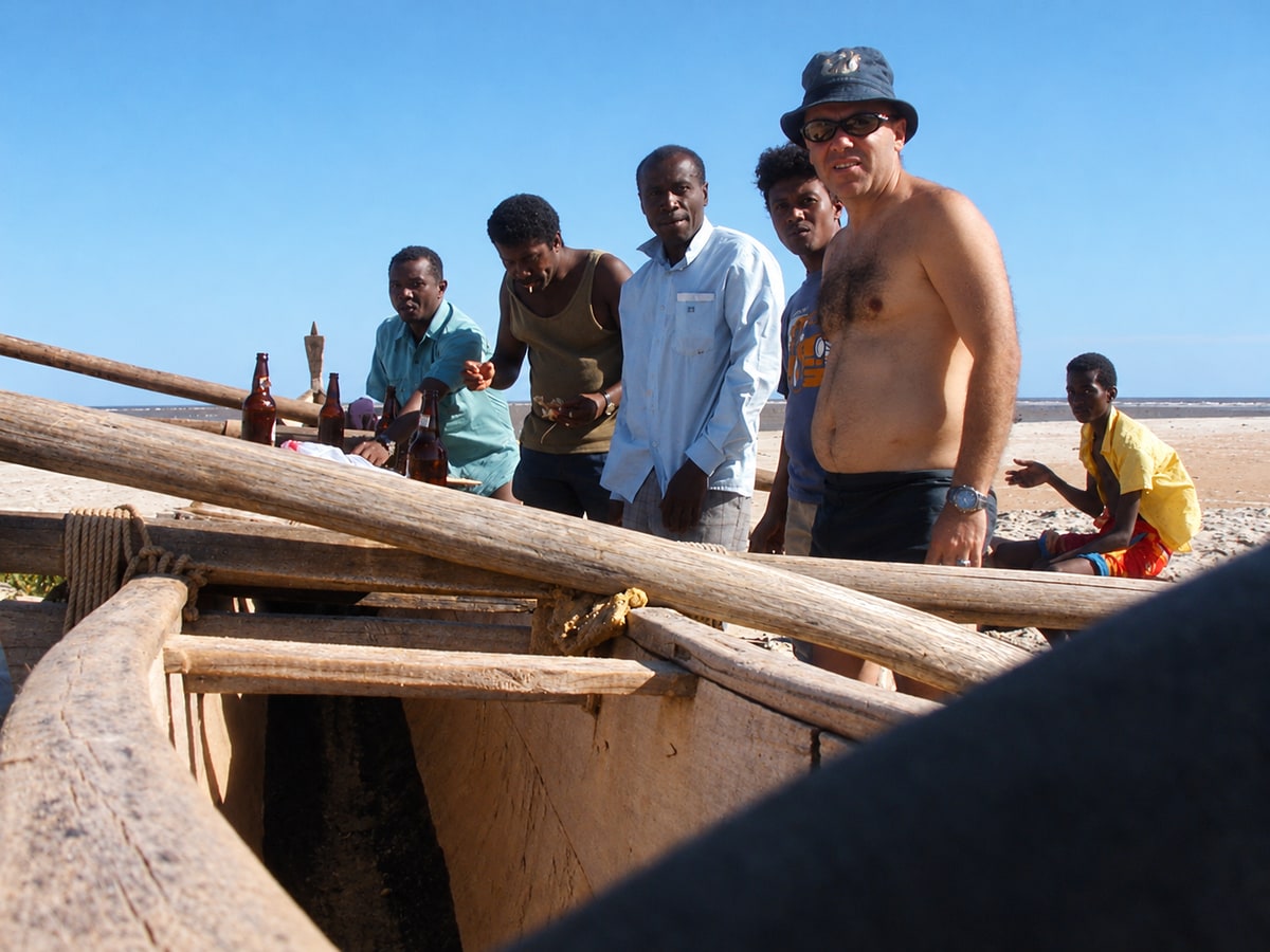 Danilo Barbero and a group near a wooden boat on a sunny shore